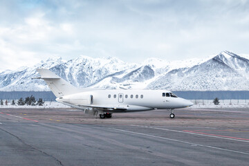 Taxiing of white luxury business jet on airport in winter on the background of high scenic snow...