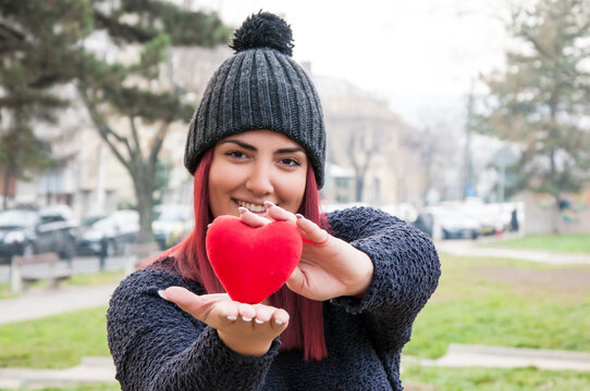 Portrait of a sedactive redhead with woolen hat in the park, holding a red heart