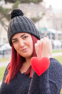 Portrait of a sedactive redhead with woolen hat in the park, holding a red heart
