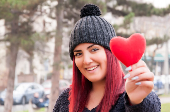 Portrait of a sedactive redhead with woolen hat in the park, holding a red heart