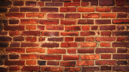 Fototapeta premium A distressed brick wall with chips cracks and stains displaying deep red and brown tones in a running bond pattern creating a vintage industrial atmosphere.