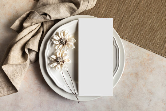 Blank menu card mockup and white flowers on plates top view, 4x9 wedding stationery card - Powered by Adobe