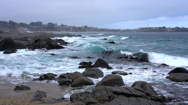 Turquoise waves crash against a rocky coastline under a cloudy sky, showcasing the power and beauty of nature