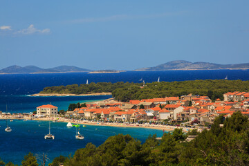 Fototapeta premium A distant view of the charming city of Primosten, Croatia, with clear blue skies and turquoise waters creating a serene coastal scene