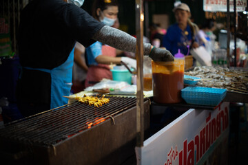 A person is cooking food on a grill, Grilled Squid. The food is being cooked on skewers and is being cooked on a grill