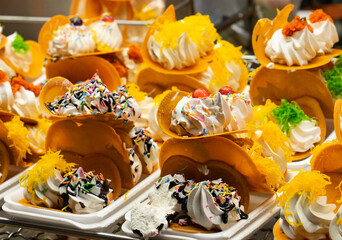 Thai Crispy Pancake. A table with a variety of desserts, including ice cream sandwiches and other treats. The desserts are arranged on a metal rack, and there are several bowls and spoons nearby