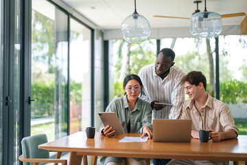 A multicultural group of young professionals interact using tablets and laptops in a well-lit office environment, clearly focused on a shared task.