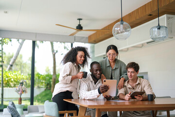 A diverse group of young adult professionals collaborates using a tablet in a bright office environment, dressed in smart casual attire, discussing ideas with enthusiasm.