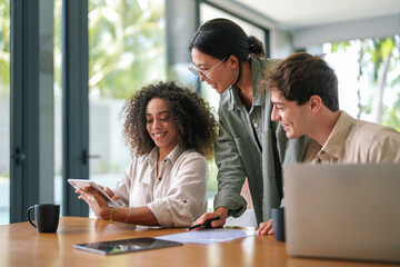 A mixed ethnicity group of young professionals collaborate with enthusiasm, using a tablet and a...