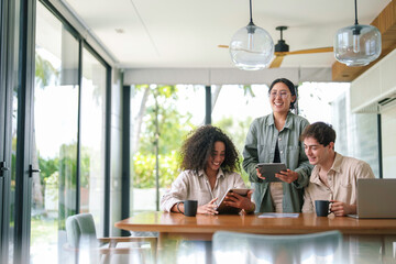 A group of young business professionals collaborates using a tablet at a wooden table in a sunlit, contemporary office space, reflecting productivity and teamwork.