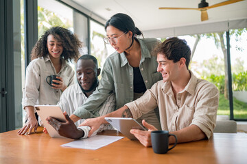 A mixed-gender group of young adults exhibits focus while collaborating around a tablet in a well-lit, modern office space, sporting casual professional attire.