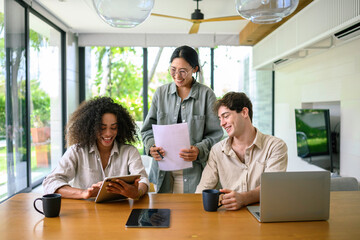 A group of happy young adults engage in a project discussion at a sleek, modern office, with...