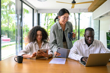 Gender-diverse and multi-ethnic group of professionals working together in a well-lit office, using laptops and digital tablets, with casual business attire.