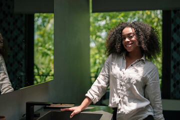 A cheerful young African American woman enjoys a sunlit bathroom, dressed casually as she rests...