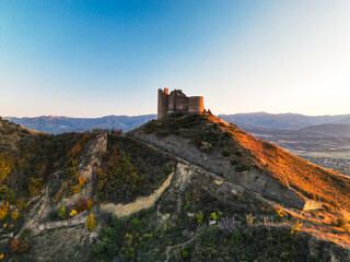 Obraz premium Ancient fantasy fortress on mountain at sunset - aerial drone view, georgia