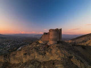 Obraz premium Ancient fantasy tower castle at sunset on desert mountain - drone aerial shot, Ksani, Georgia