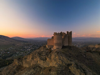 Ancient fantasy fortress on mountain at sunset - aerial drone view, georgia