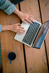 Close-up view of a woman's hands typing on a laptop, indicative of remote work from home, with a coffee cup beside her on a wooden table.