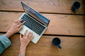 A woman works from home, her hands poised over a laptop keyboard, with a coffee mug nearby on a...