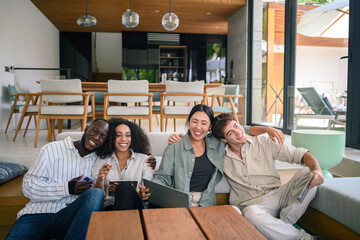A diverse group of young adult professionals engages in a collaborative work session on comfortable seating, using a laptop and mobile devices in a stylish office environment.