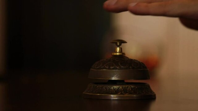 call on a old hotel bell on a wood stand. the visitor's hand calls the concierge at the hotel reception in the reception bell. at first once, then repeatedly presses the button