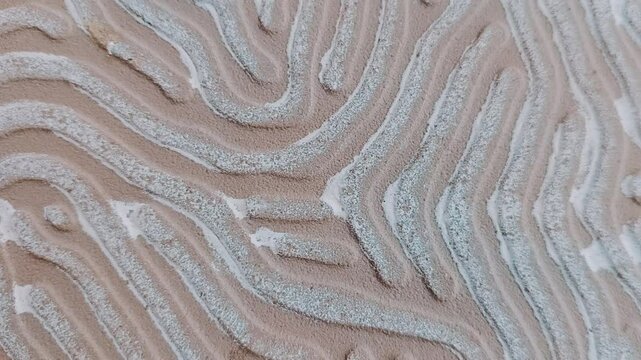 The winding lines pattern with a rough texture in cream and white, resembles the natural pattern on sand or the ground surface. At the bottom, there is a media player control display.