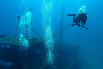 Underwater photographer adjusting camera settings, rusty wreck and air bubbles. Scuba diving...