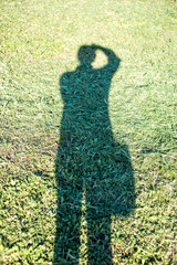 shadow of a man with a camera against the background of mown green grass.