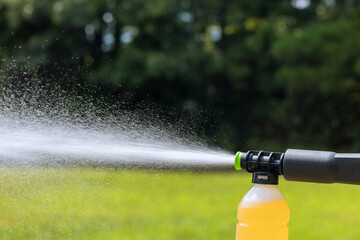 Garden nozzle sprays fine mist of cleaning solution onto grass in backyard.