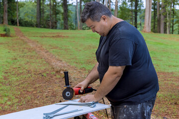 Craftsman is focused on using an angle grinder to cut through piece of metal while working outside
