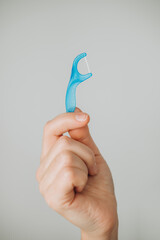 Holding a blue dental flosser against a light gray background in a well-lit setting