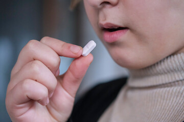 Close up image of a girl  taking white round pill. Young girl taking medicines, antidepressant.
