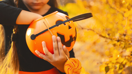 Close-up portrait of a 4-5 year old girl in a witch costume with a candy bucket against a...