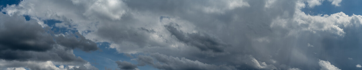 Very wide panorama of a summer cloudy sky with patches of light blue

