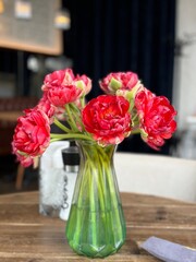 Vibrant red tulips in a green glass vase on a rustic wooden table indoors