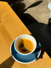 Morning espresso in a blue cup with natural sunlight casting shadows on a wooden table