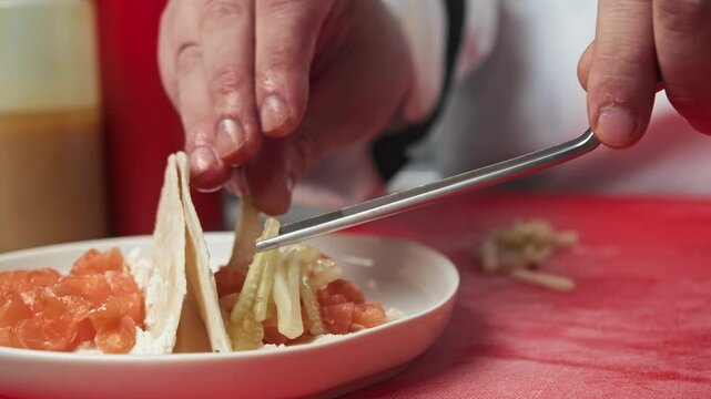 Chef adds sliced cucumber, without the peel, to Mexican dish of tacos with amenable red salmon fish in gourmet restaurant.