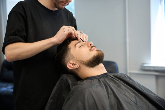 Expert groomer applies wax for hair removal between client brows