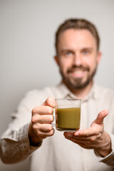 Kratom consumption concept:  male bearded hipster holds a ready to drink glass of green liquid, powdered kratom melted in hot water, kratom tea, close up photo, selective focus