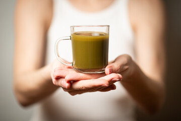 Kratom consumption concept:  female holds a ready to drink glass of green liquid, powdered kratom...