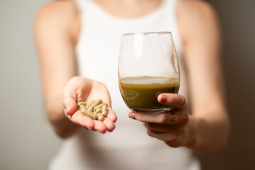 Kratom consumption concept:  female holds a ready to drink glass of green liquid, powdered kratom...