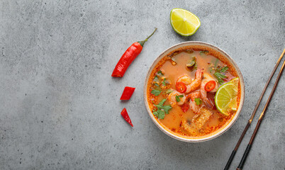 Traditional spicy thai soup tom yum served with shrimps, lime, chili pepper and coriander in bowl...