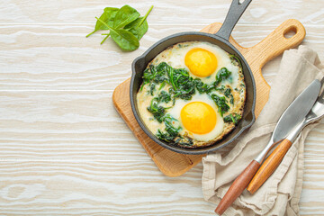 Healthy spinach omelette with two fried eggs in a cast iron pan, served on a wooden table with...