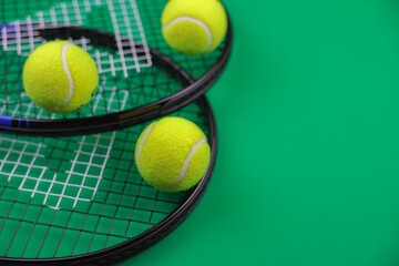 Top view on a green background, two tennis rackets for lawn tennis are lying on the side, yellow tennis balls with a place for text on the side are on top of them. High quality photo