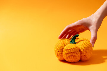 crocheted pumpkin in female hand on yellow background, copy space