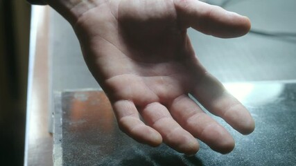 Man holds shaky hand over empty metal desktop in workshop closeup. Worker shows symptom of chronical tiredness and stress at workplace. Hypoglycemia symptoms.
