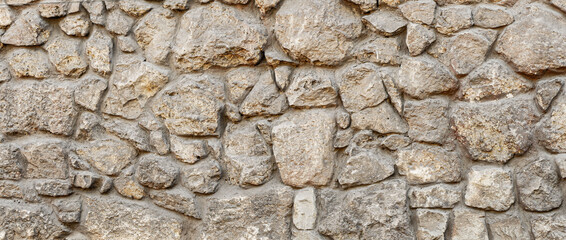 Old coarse pattern panoramic stone wall made of various square natural stones and blocks in beige,...