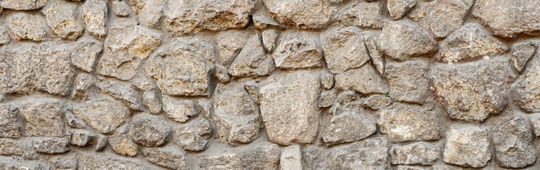 Old coarse pattern panoramic stone wall made of various square natural stones and blocks in beige,...