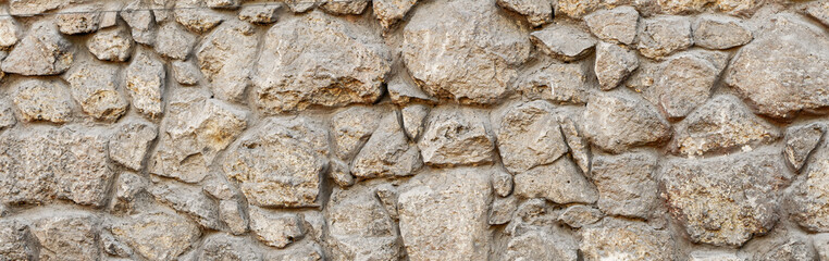 Old coarse pattern panoramic stone wall made of various square natural stones and blocks in beige,...