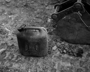 a fuel canister on the ground next to a backhoe bucket.